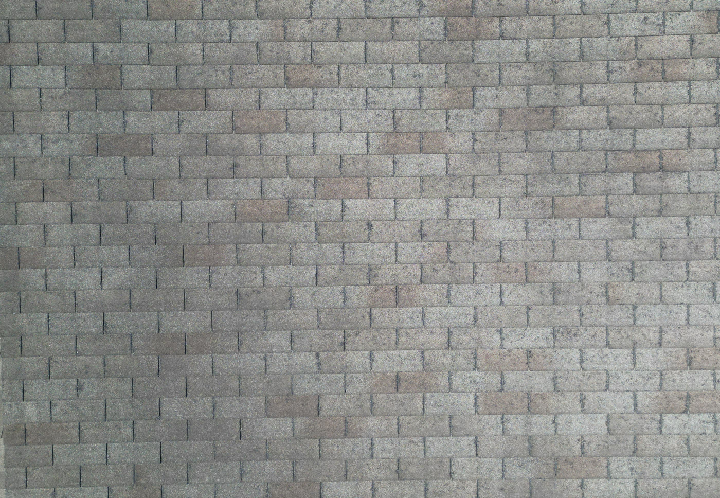 Close-up aerial view of an asphalt shingle roof surface, the detail where hail impacts and granule loss are inspected