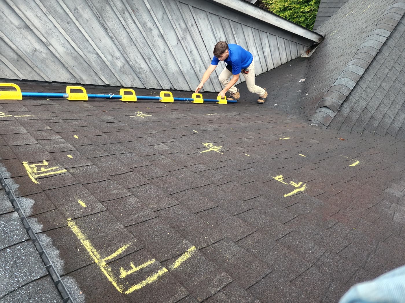 A RuFR USA inspector documenting a roof for an insurance claim, with hail strikes chalk-marked on the shingles and a chalk line for scale